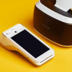 Terminal de paiement intelligent blanc et casque de réalité virtuelle sur fond jaune moderne.