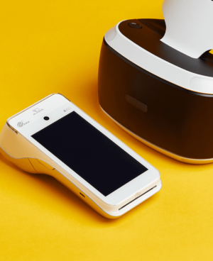 Terminal de paiement intelligent blanc et casque de réalité virtuelle sur fond jaune moderne.