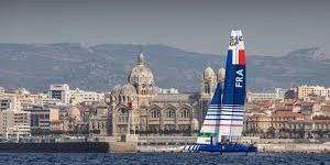 Catamaran français naviguant devant la Cathédrale La Major à Marseille.