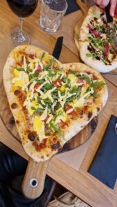 Pizza en forme de cœur avec roquette et tomates sur planche en bois rustique.