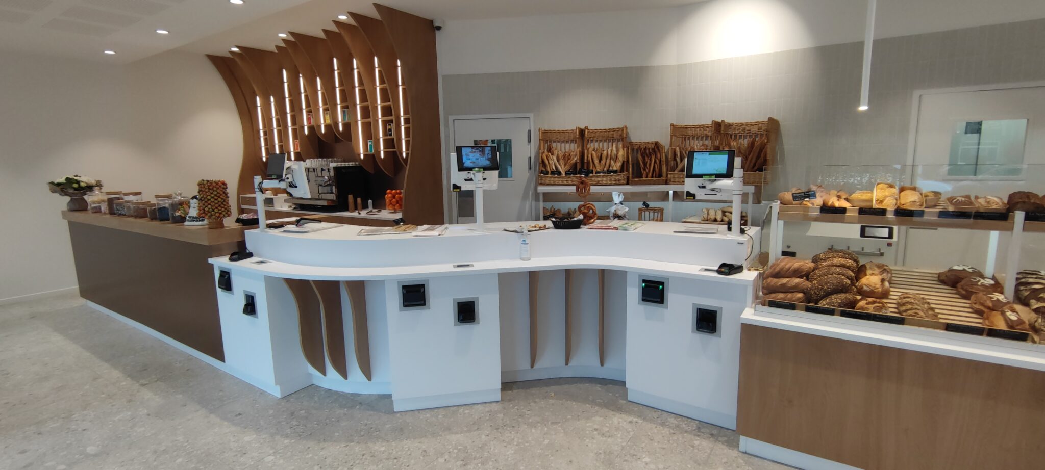 Intérieur de boulangerie moderne avec comptoir en bois clair, pains artisanaux et viennoiseries fraîches.